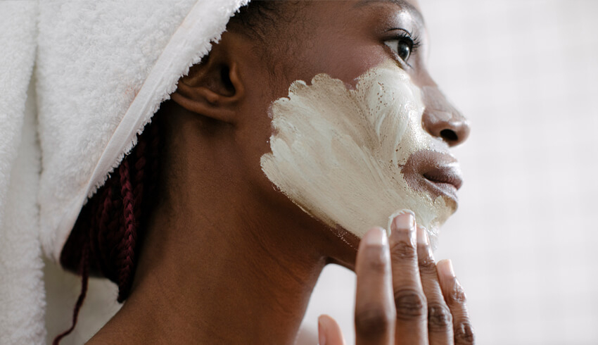A woman applying a face mask to her face.